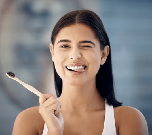 Young woman holding a bamboo toothbrush with a black head.