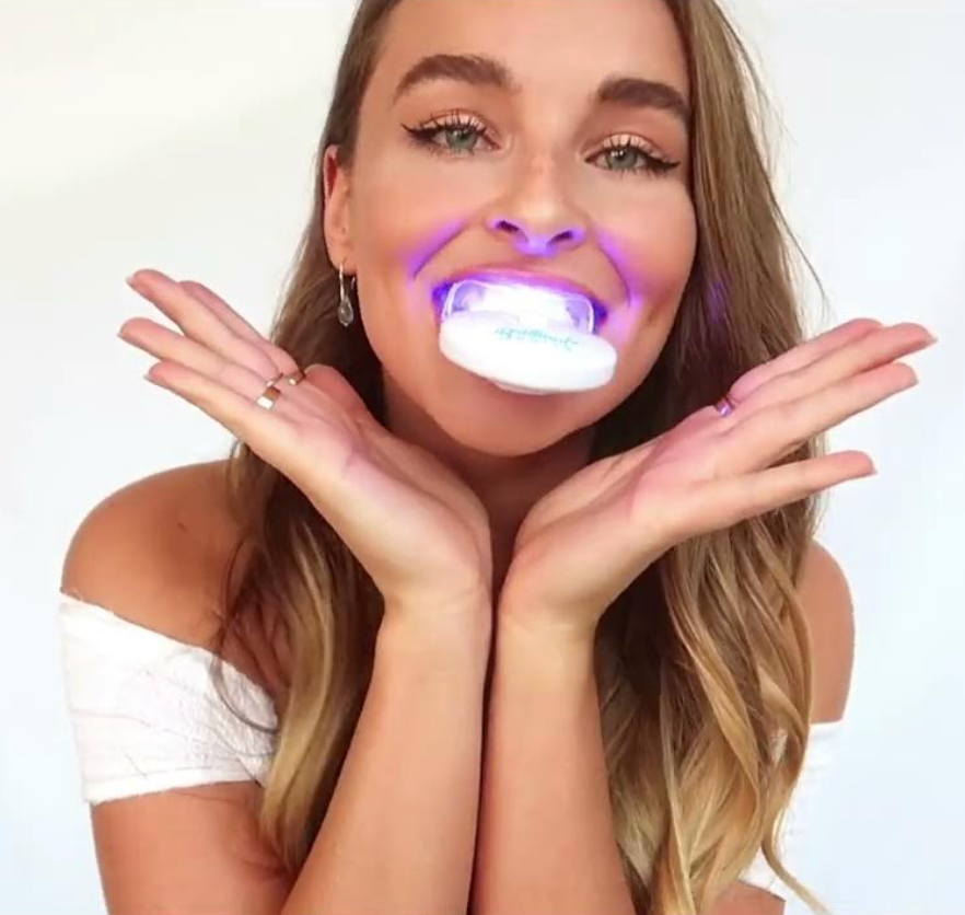 A young woman using an LED apparatus to whiten her teeth